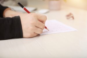 Student hand filling in exam paper with pencil.