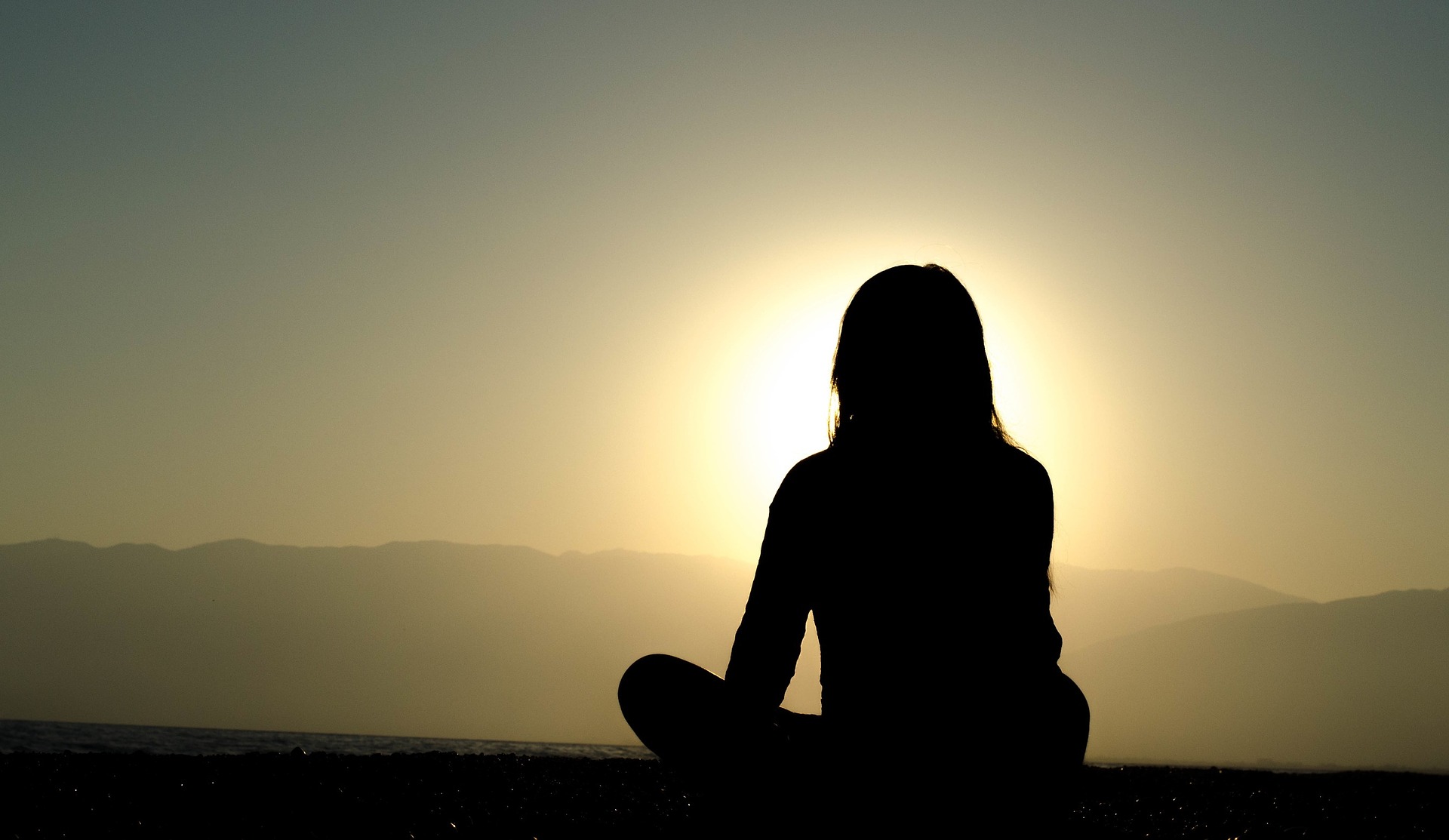 Woman sitting atop a mountain overlooking peaceful surroundings.