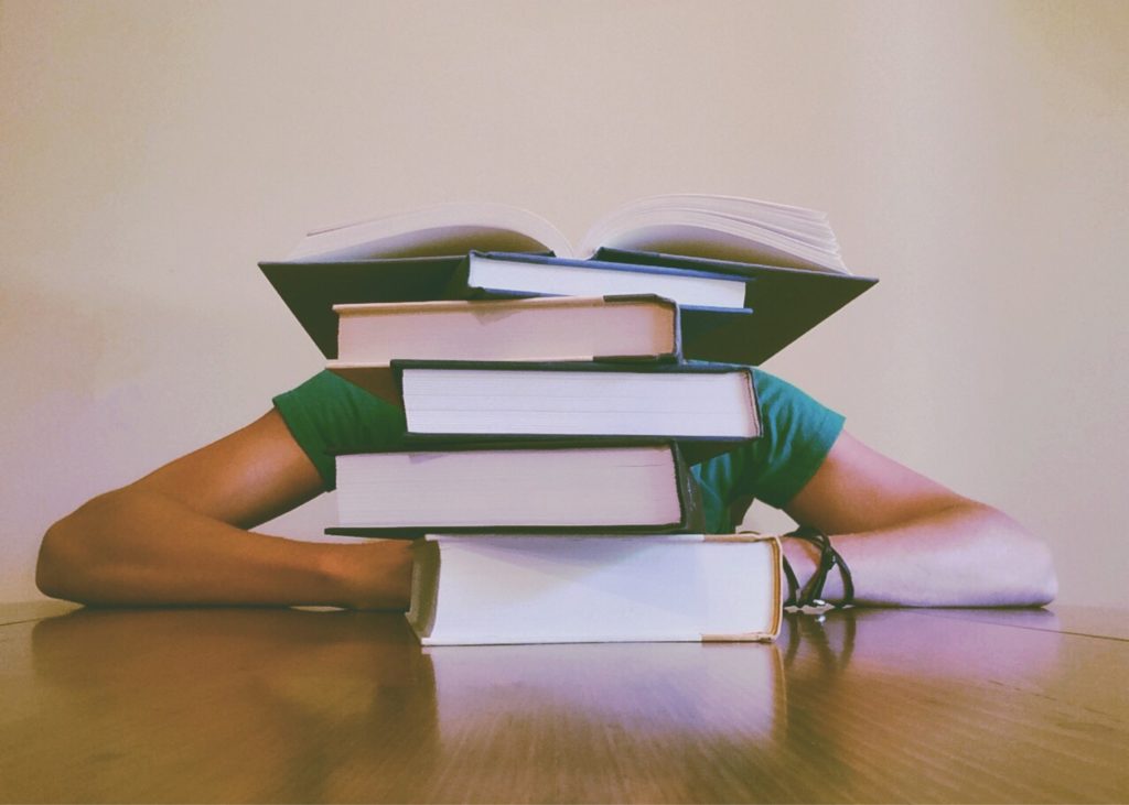 Woman behind stack of books to study.