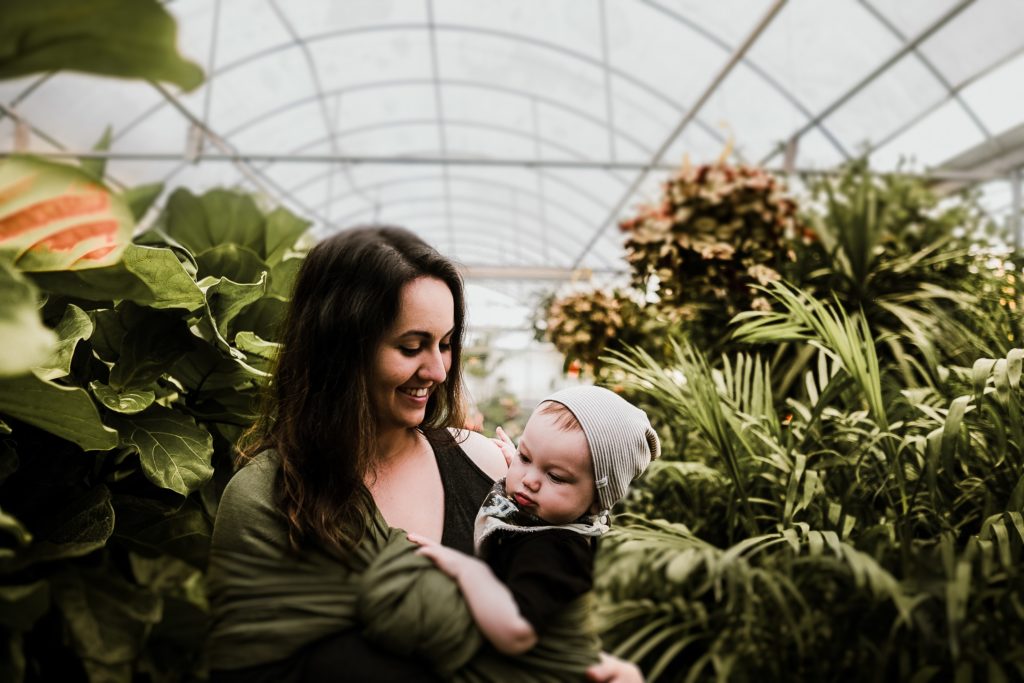 Mom babywearing in a greenhouse.