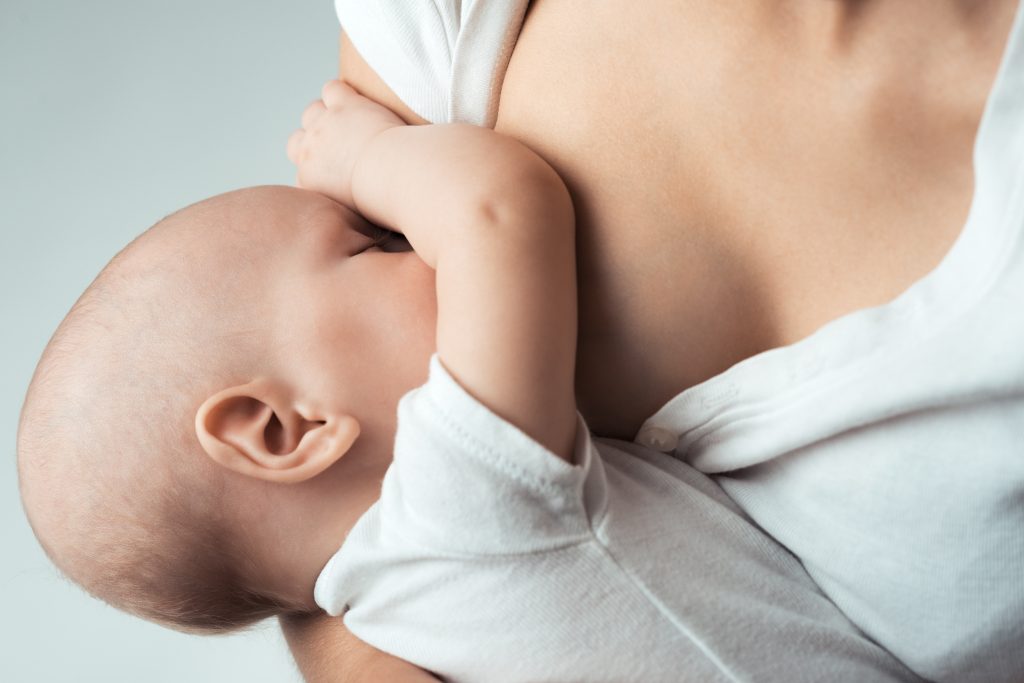 Mother in white top breastfeeding her child in a white onesie,