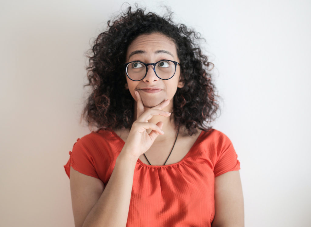 Woman in red shirt looking up in contemplation with hand on chin.