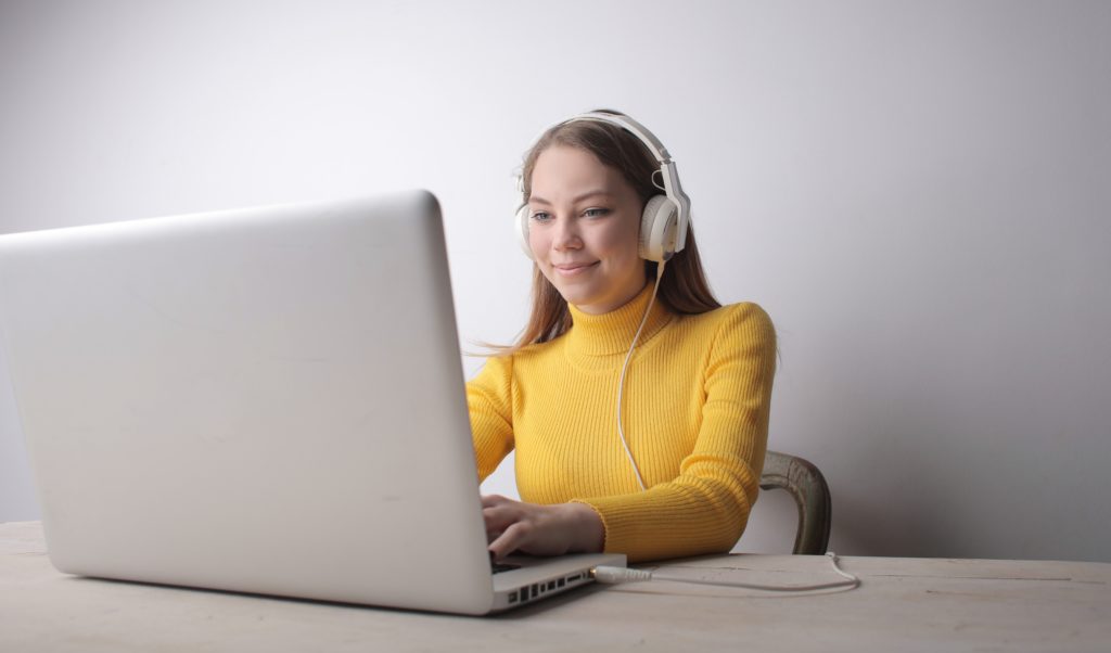 Woman in yellow wearing headphones at laptop.