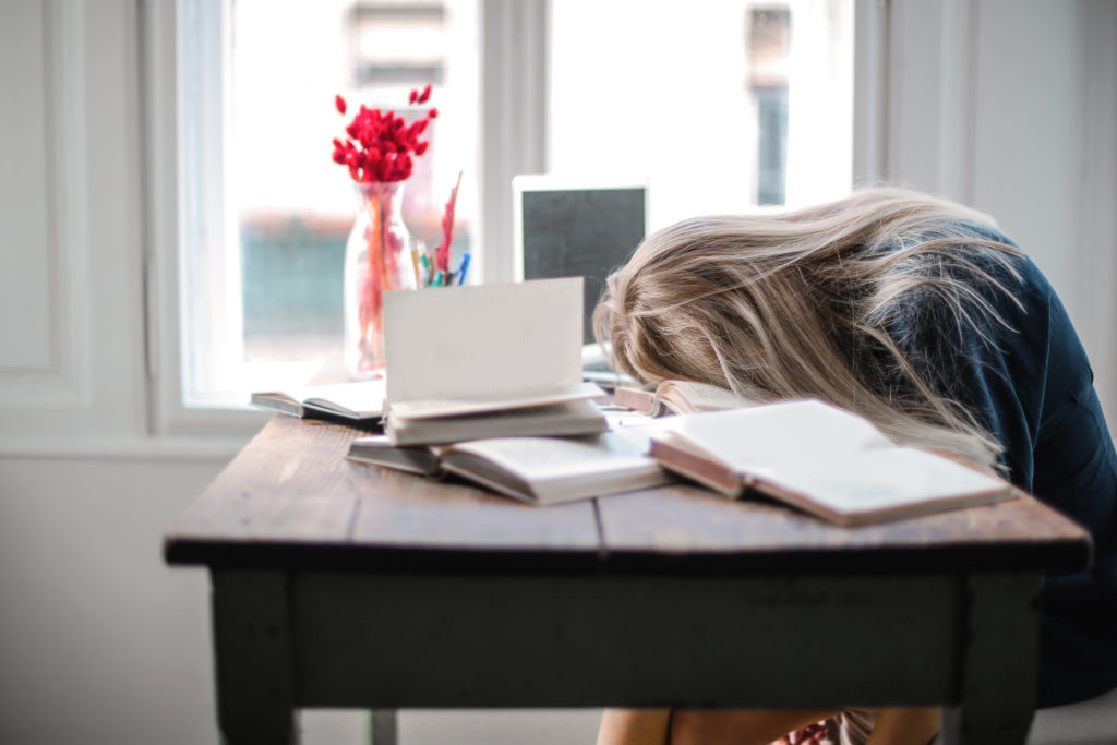 Woman with head on desk who needs to stop procrastinating and start studying