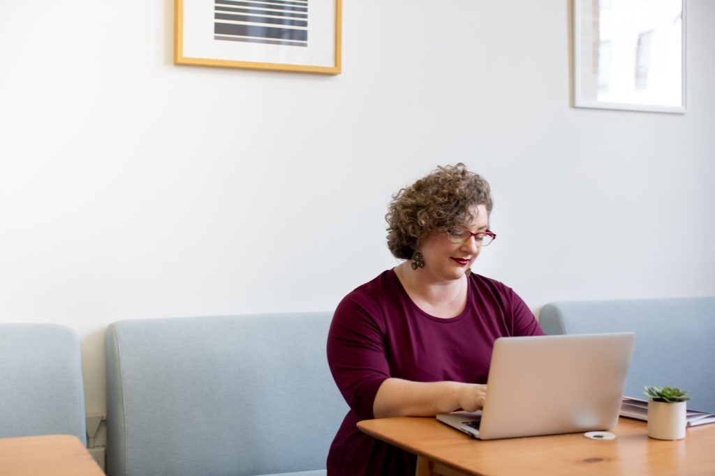 Woman in burgundy searching for practice exams on a laptop.