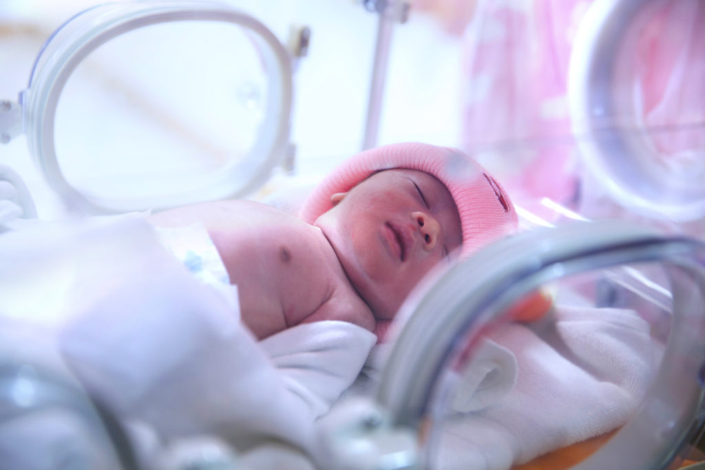 Baby with pink hat in NICU isolette