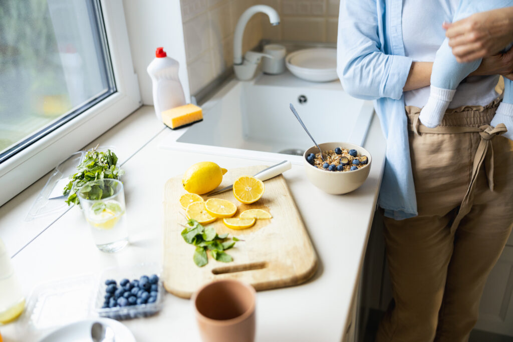 Mom holding infant doing meal prep for the right postpartum diet.