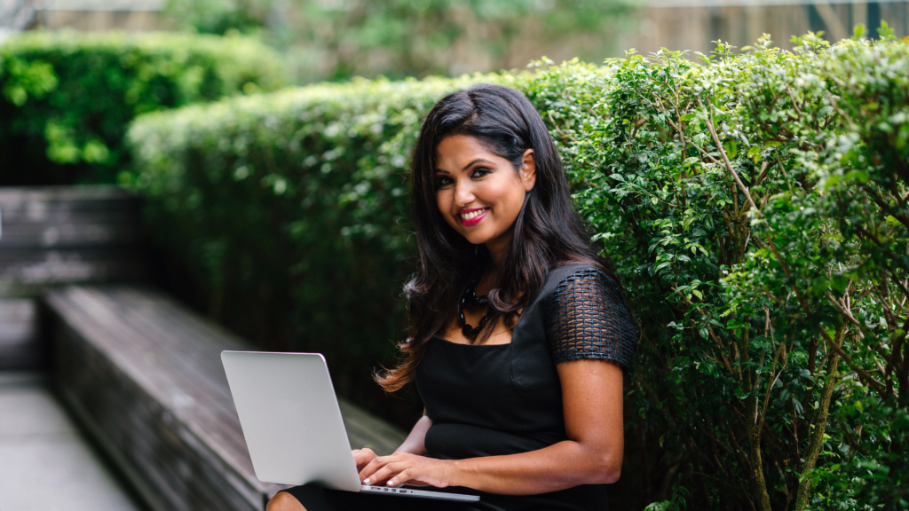 Woman in black dress sitting outside with laptop computer.