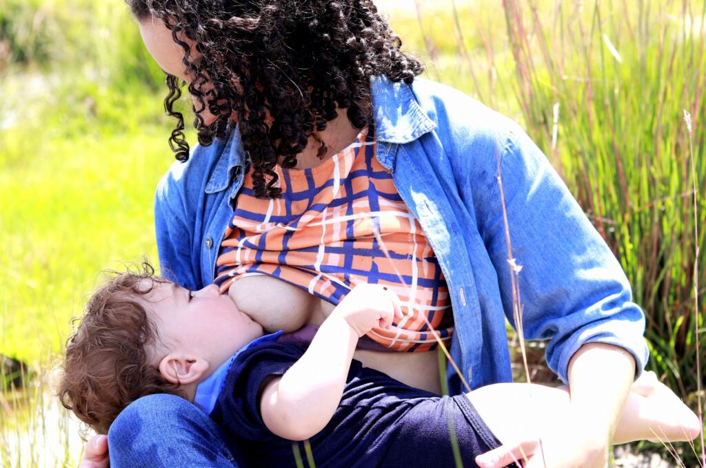 Brunette woman in blue shirt breastfeeding in a field of green grass.