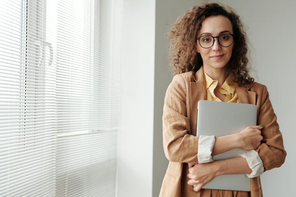 Woman holding laptop in front of an office window.