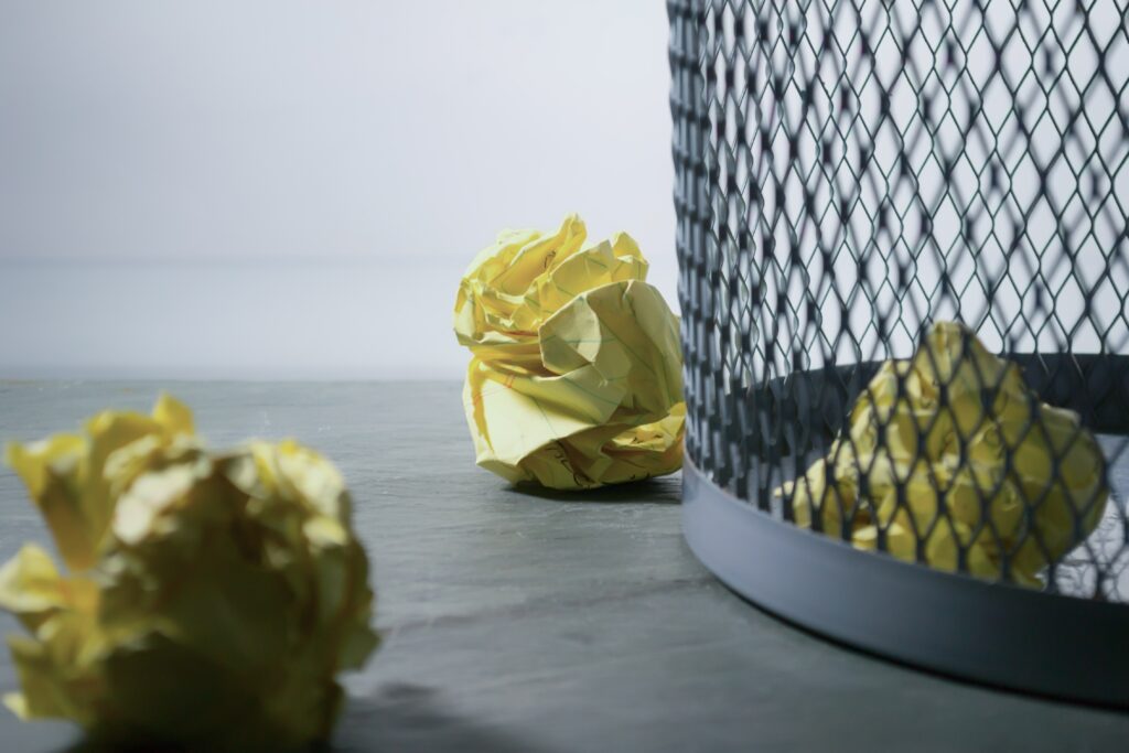 Wire waste basket with crumpled yellow paper.