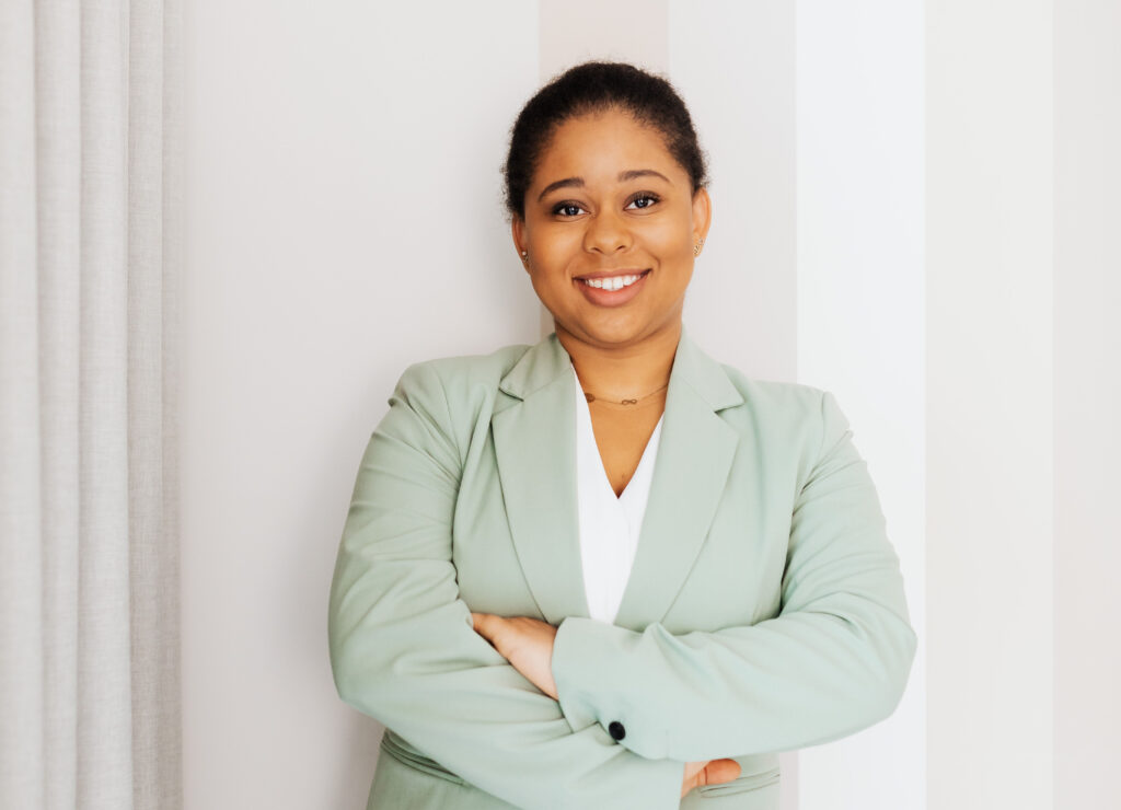 Woman in green blazer up standing against a striped wall.