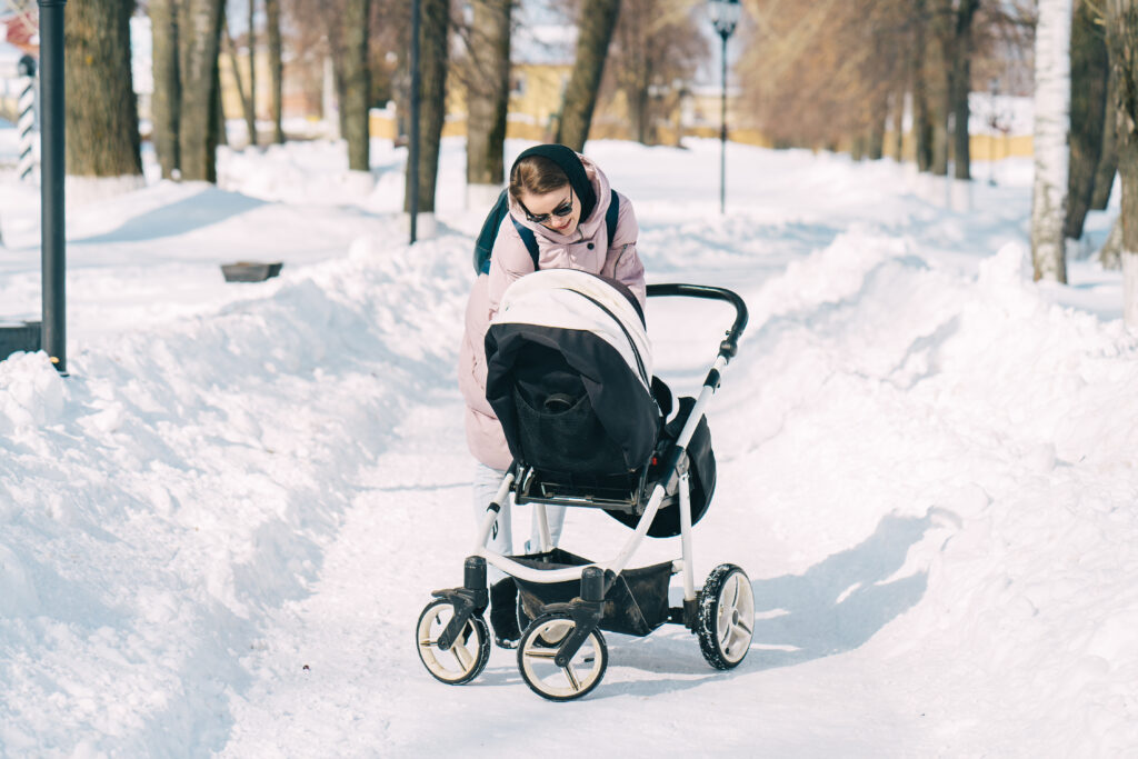 Woman with stroller on snow-covered sidewalk.