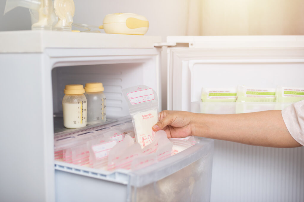 Hand reaching into freezer full of milk storage bags and containers of milk.