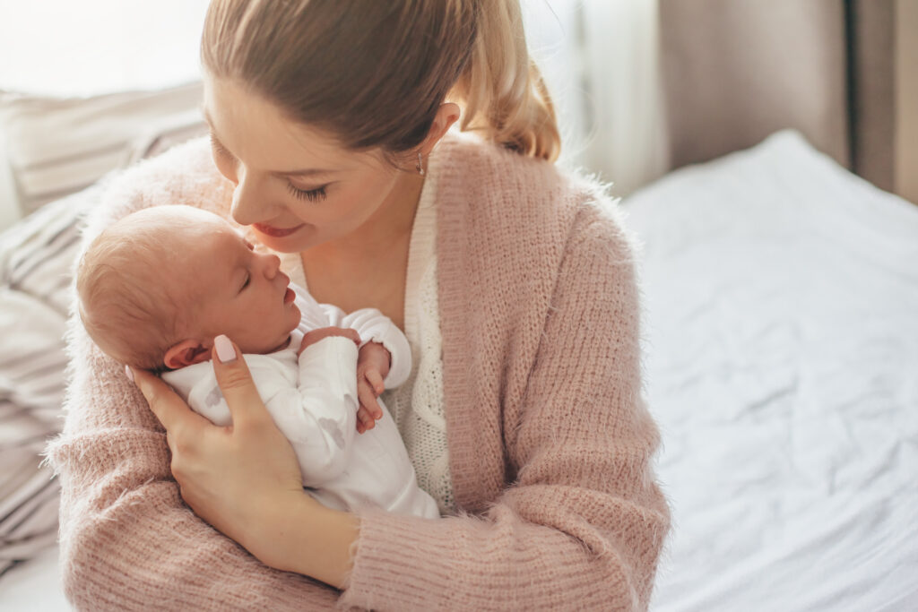 Mother in pink sweater holding newborn infant on hospital bed.