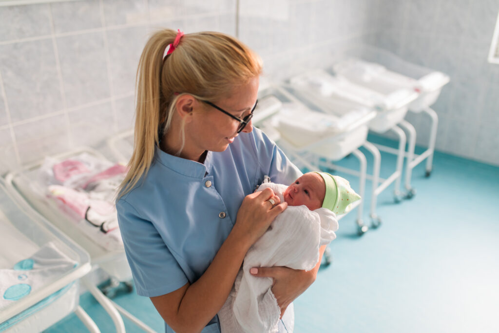 Nurse in hospital nursery holding newborn infant.
