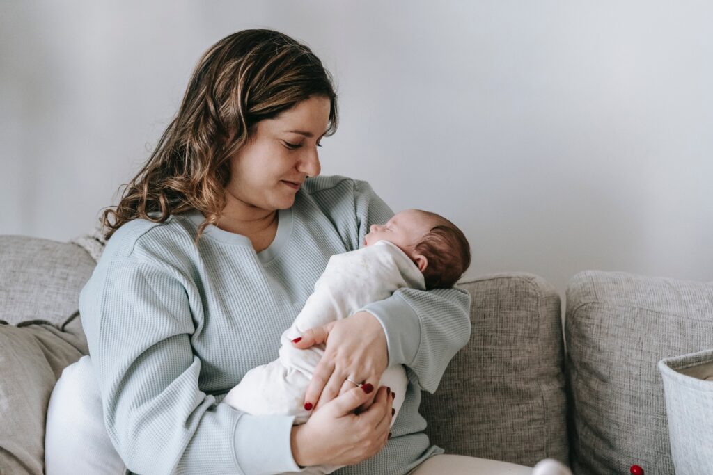 Brunette woman holding newborn infant on a couch.