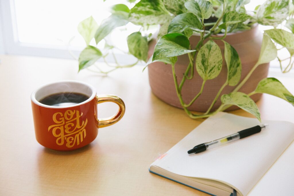 Red mug with "Go get 'em" text alongside a plant and notebook for planning.