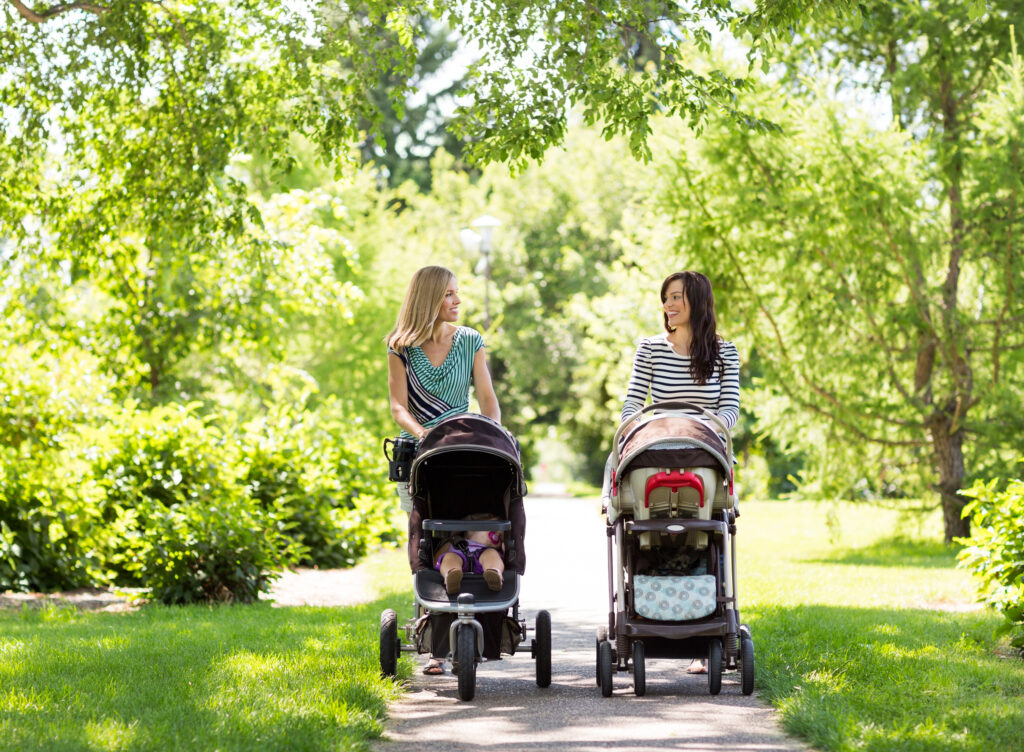 Two woman pushing strollers outdoors.