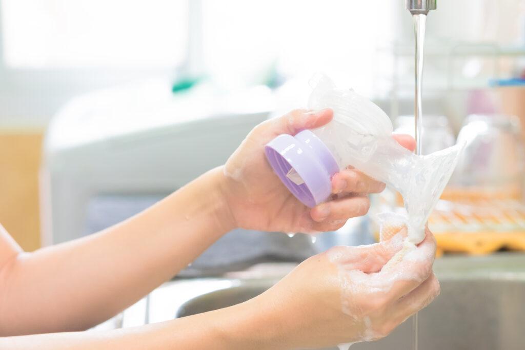 Hands washing breast pump parts in a sink.