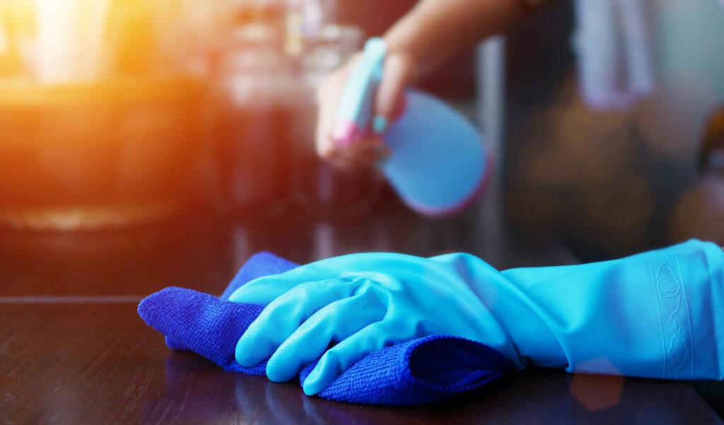 Gloved hands spraying and wiping down counter for cleaning and sanitizing. 