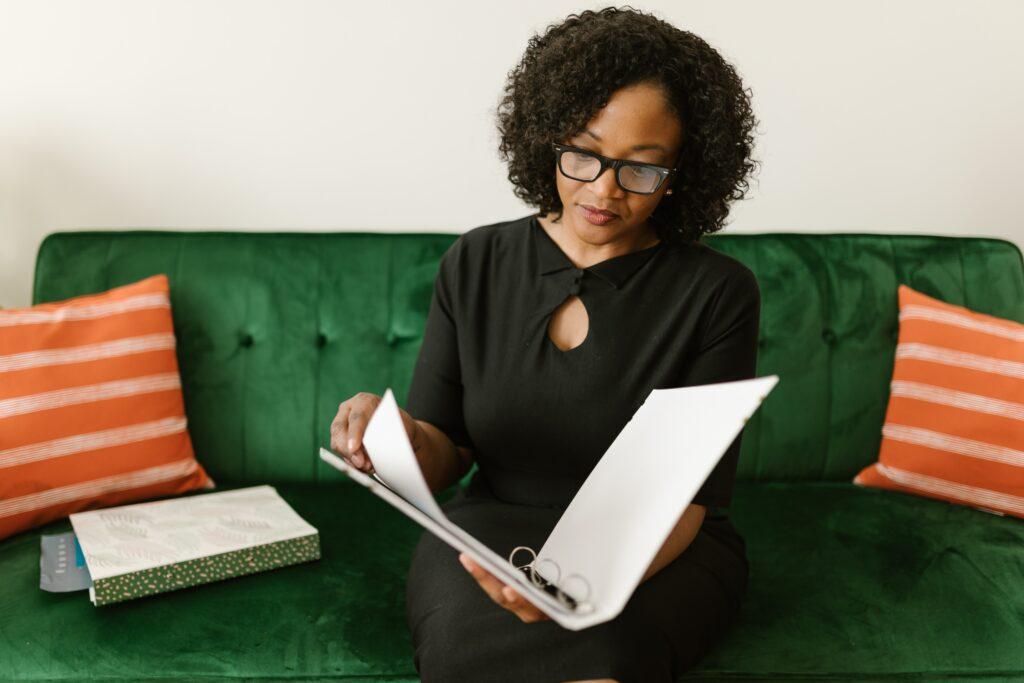 Woman on green couch looking at papers in a binder.