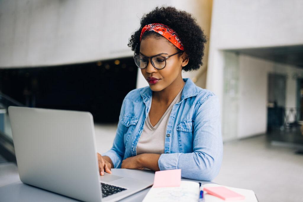 Black woman sitting at a laptop computer with notes nearby.