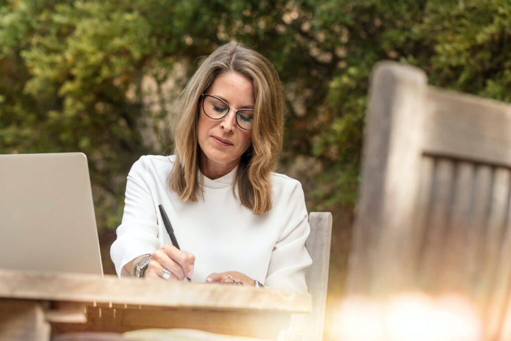 Woman sitting at an outdoor table with laptop computer and notebook. 