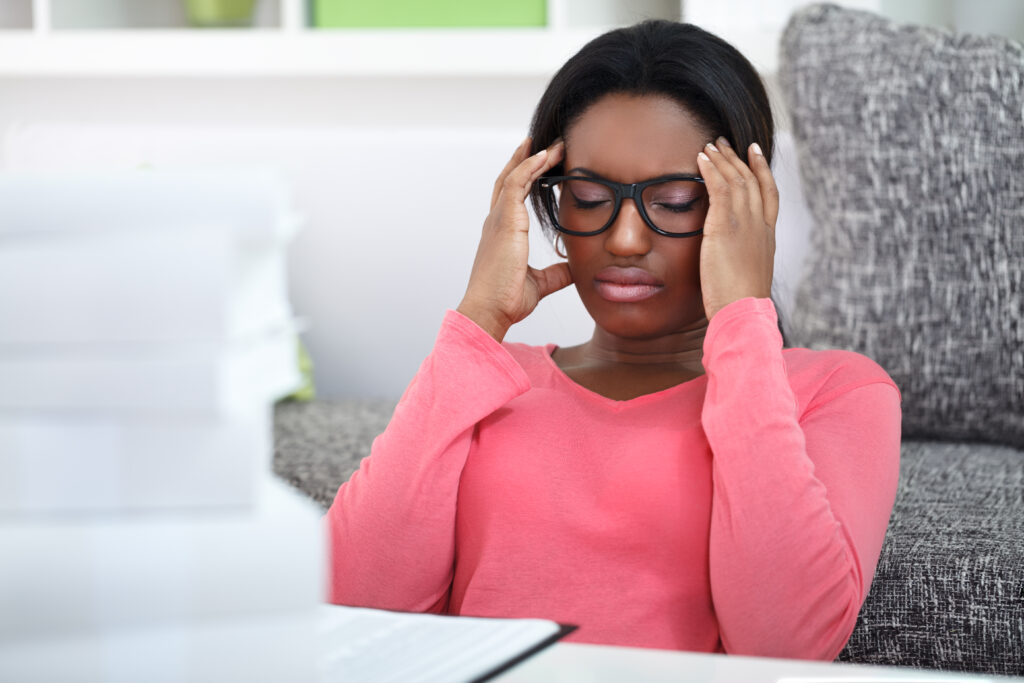 Black woman in pink shirt rubbing her temples in front of a stack of books struggling with test anxiety.