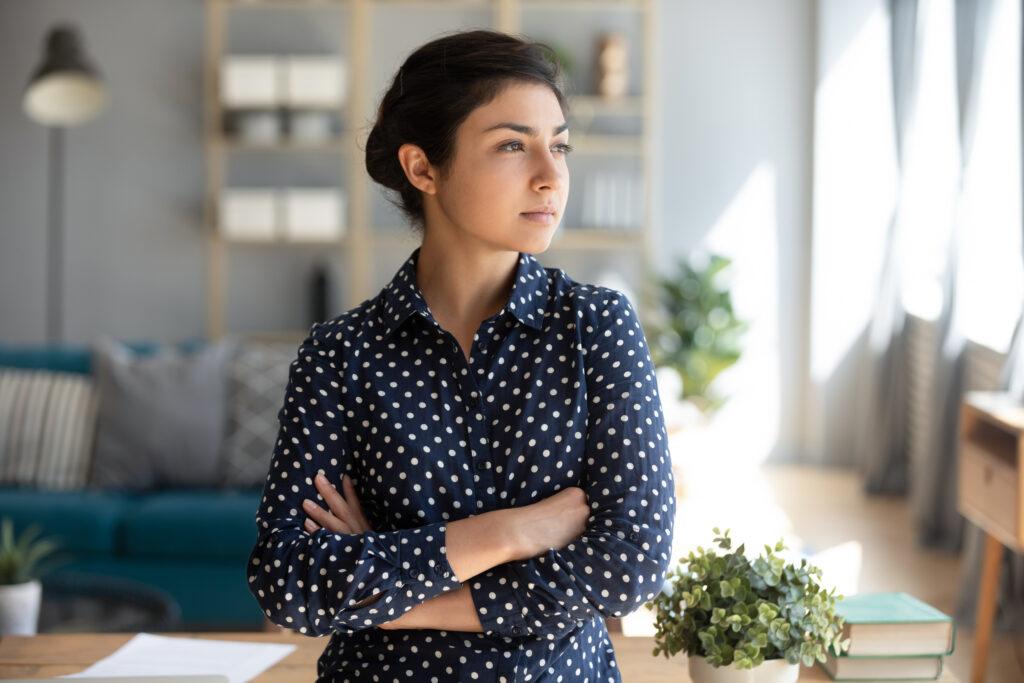 Woman in navy polka dot shirt looking out window.