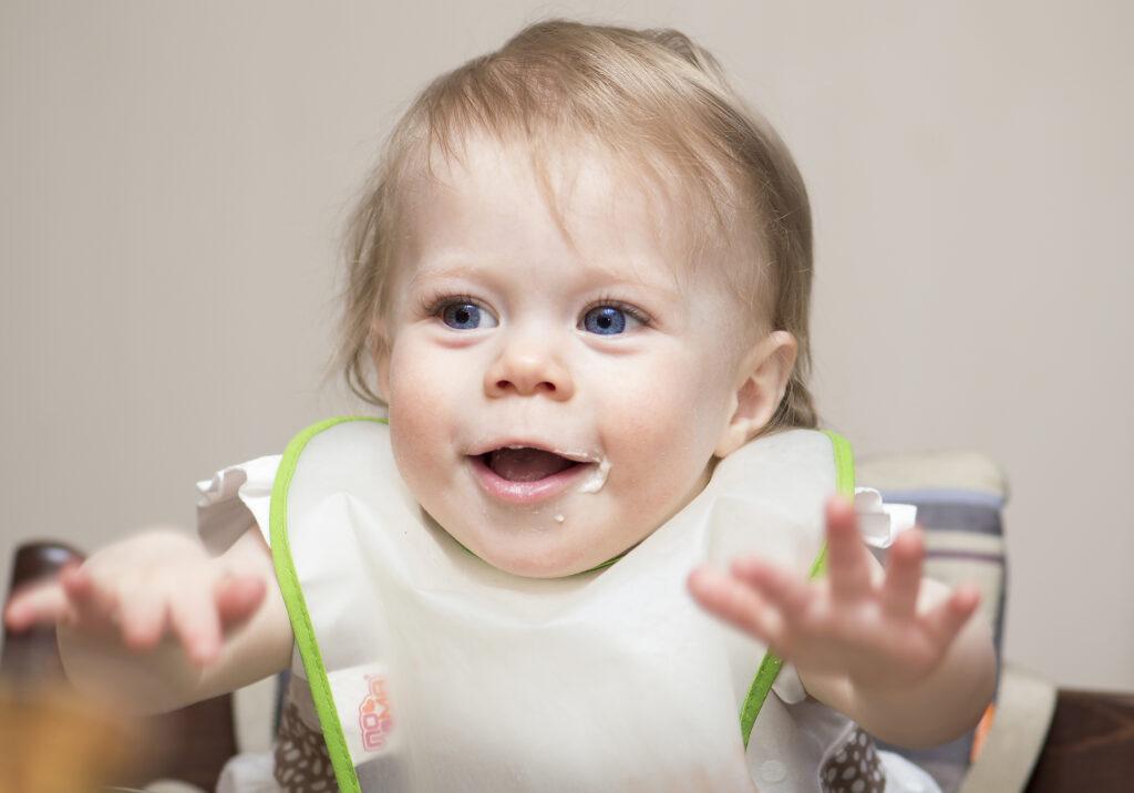 Hungry infant in high chair wearing a bib.