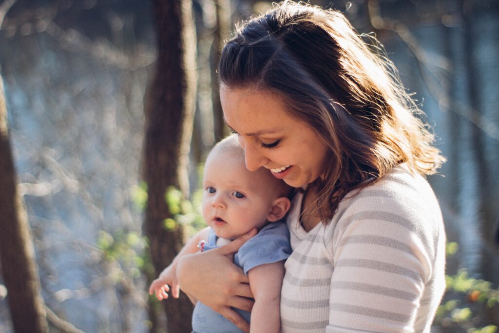 Smiling mom holding young baby in blue shirt.