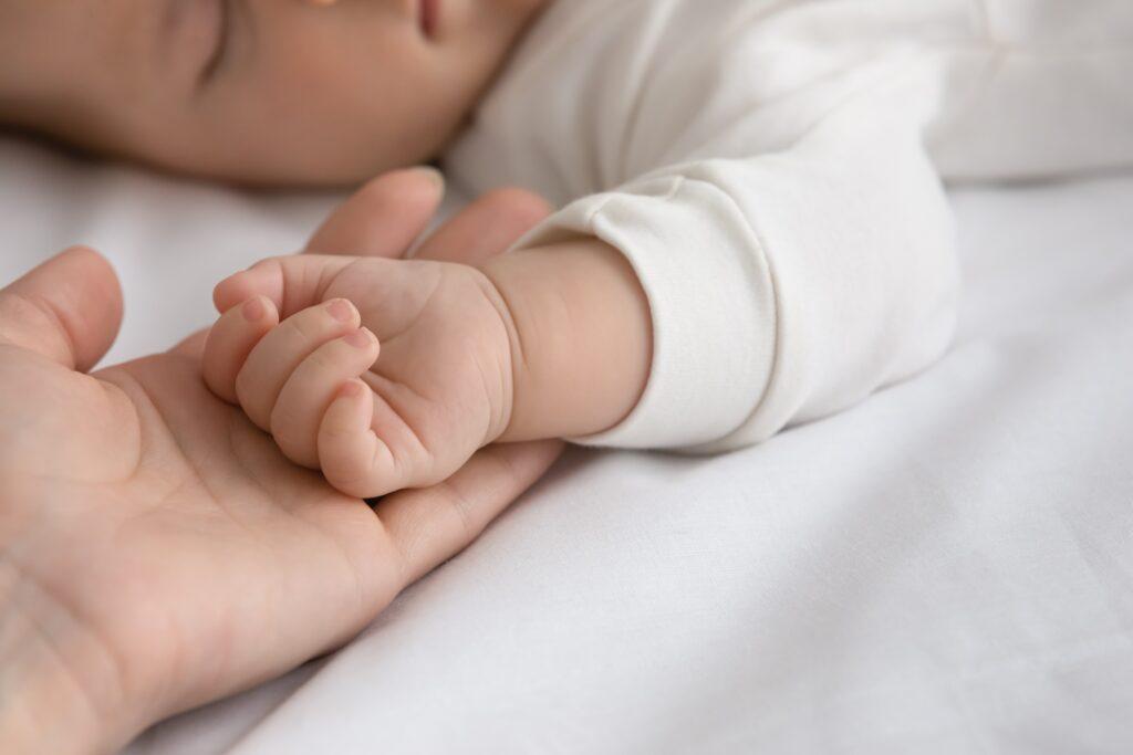 Adult holding newborn hand during sleep.