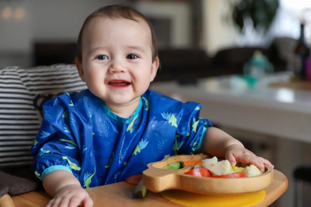 Happy baby wearing a blue bib while sitting in a high chair. 