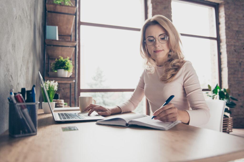 Woman at desk working through a process with computer and notebook.