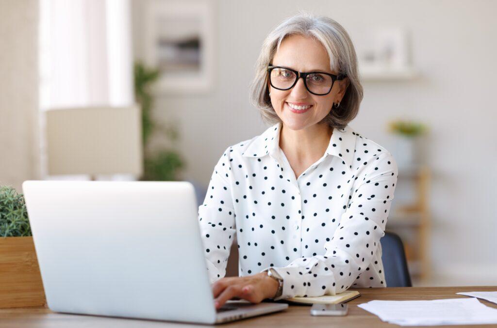 Smiling woman in polka dot shirt in front of computer.