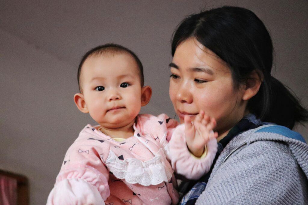 Asian mom holding baby dressed in pink.