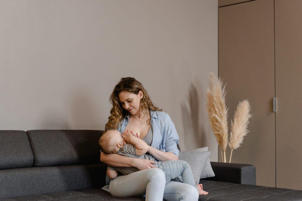 Mom sitting on couch with baby on lap breastfeeding.