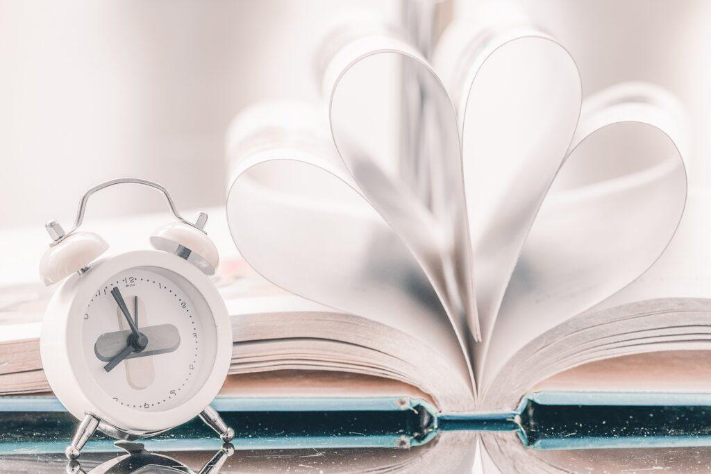 White alarm clock in front of book with curved pages. 