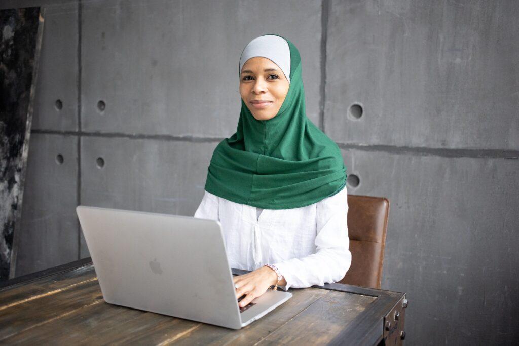 Woman in green head covering working at laptop computer.