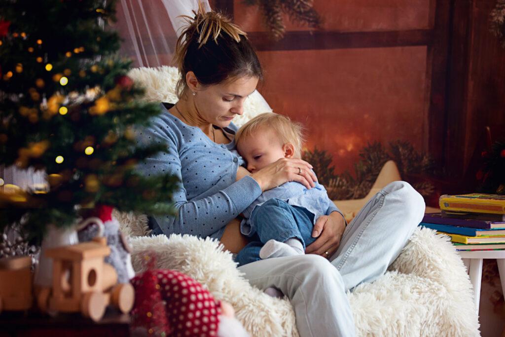 Woman breastfeeding next to a Christmas tree during the holidays.