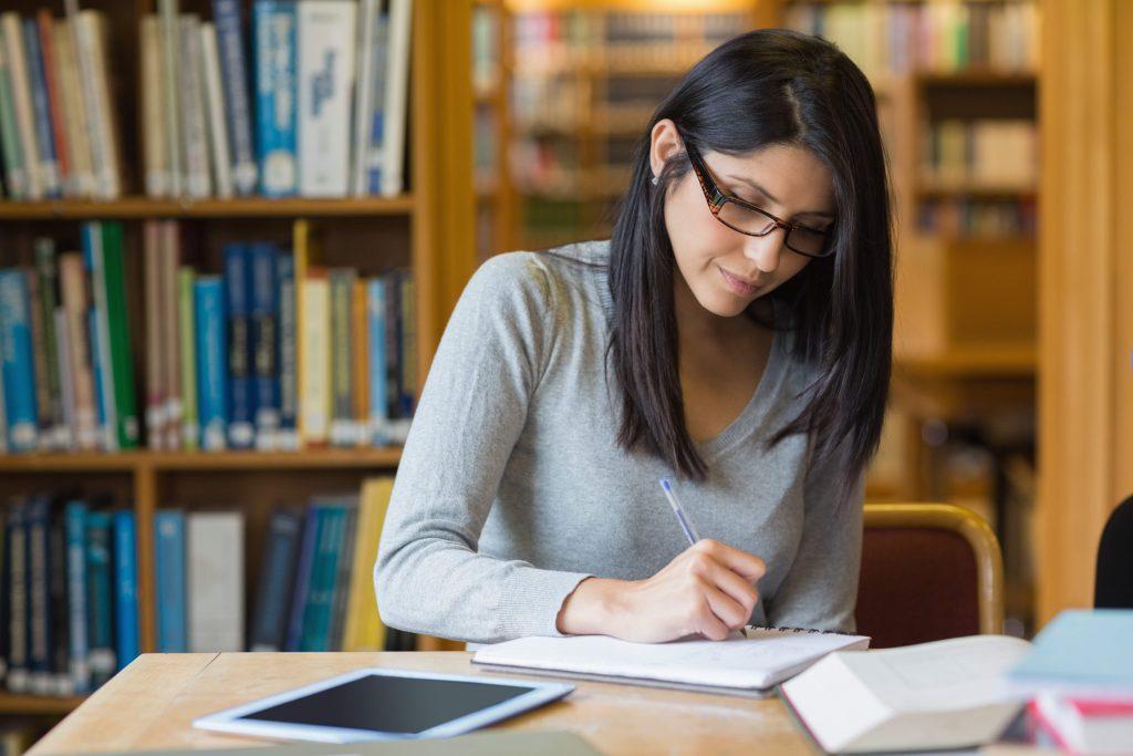 Woman sitting at a library writing while studying.