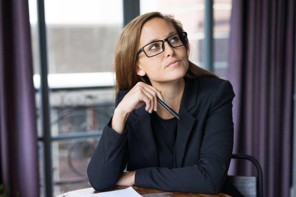 Woman with glasses looks into the distance in thought after taking the IBCLC exam. 