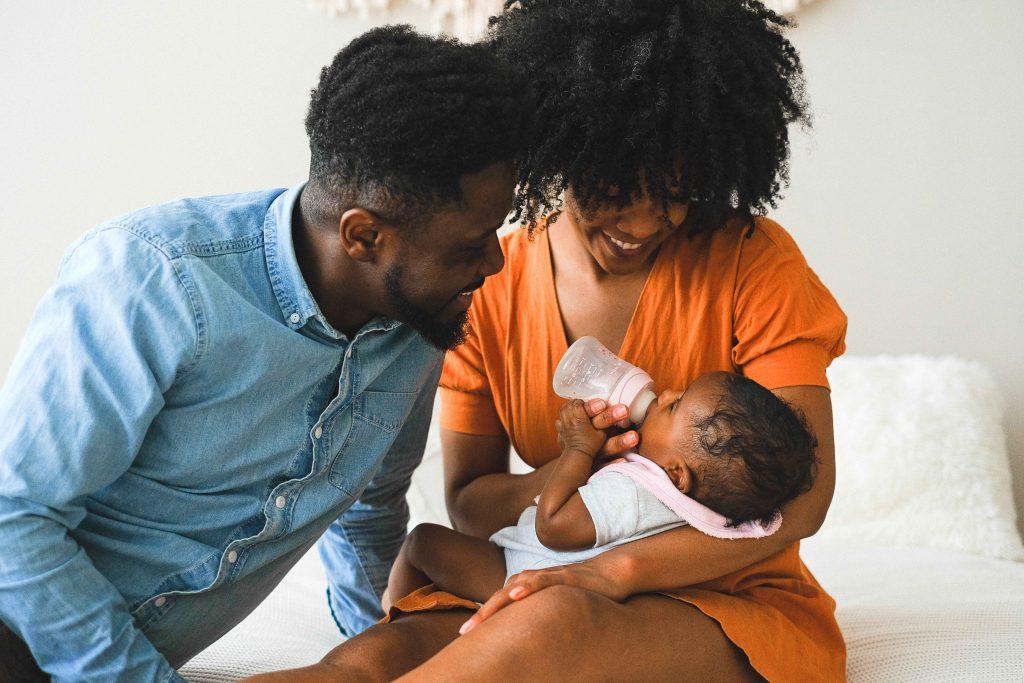 Black couple holding baby that is bottle feeding.