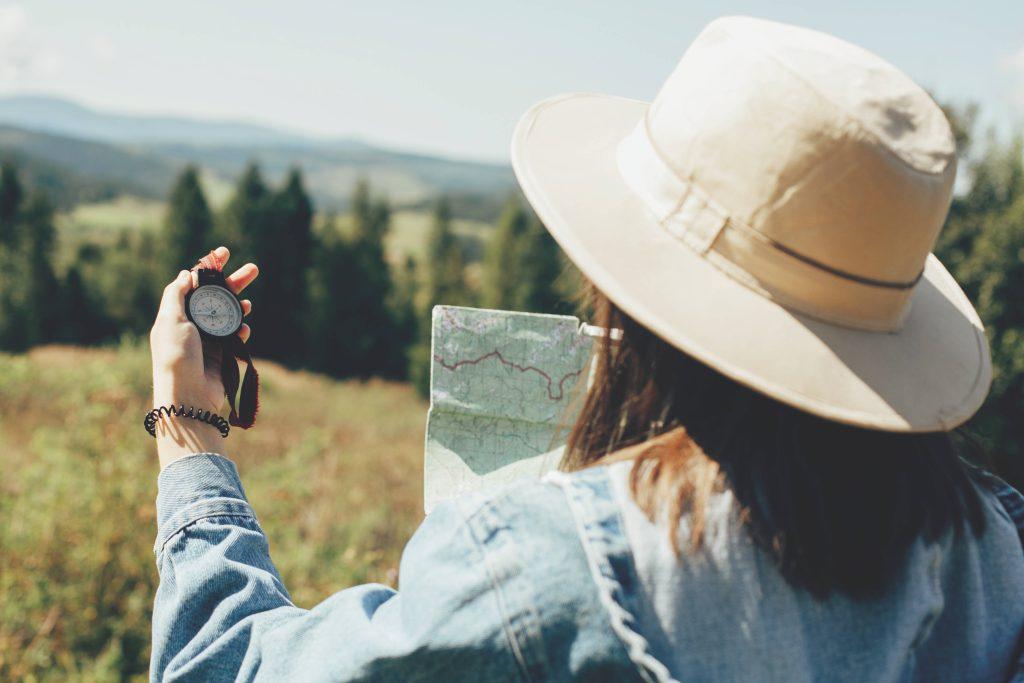 Woman wearing hat outdoors holding a map and compass.