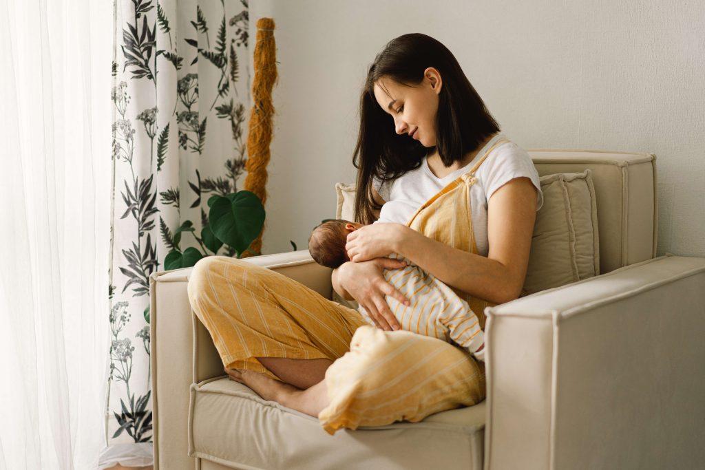 Woman sitting on chair near window breastfeeding a baby.