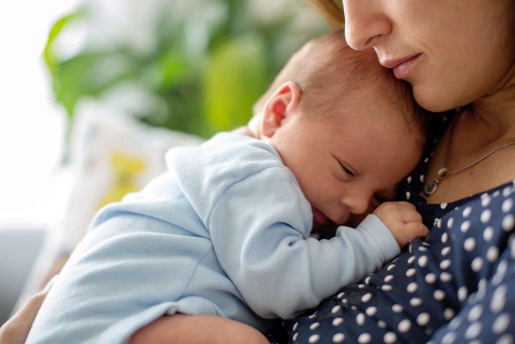 Woman in polka dot shirt holding baby wearing blue.