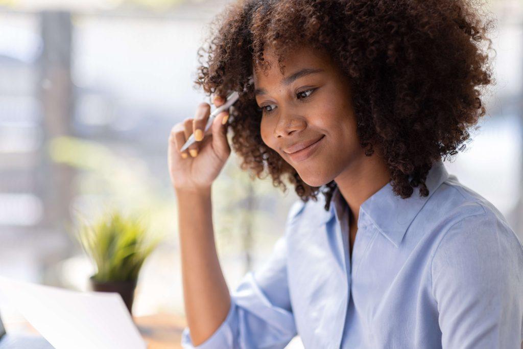 Smiling woman in blue shirt looking at paper while holding a pen. 