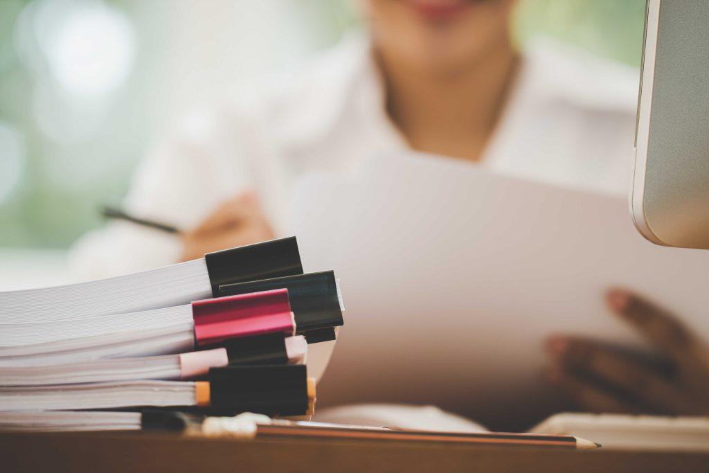 Woman in background with books and papers in the foreground.