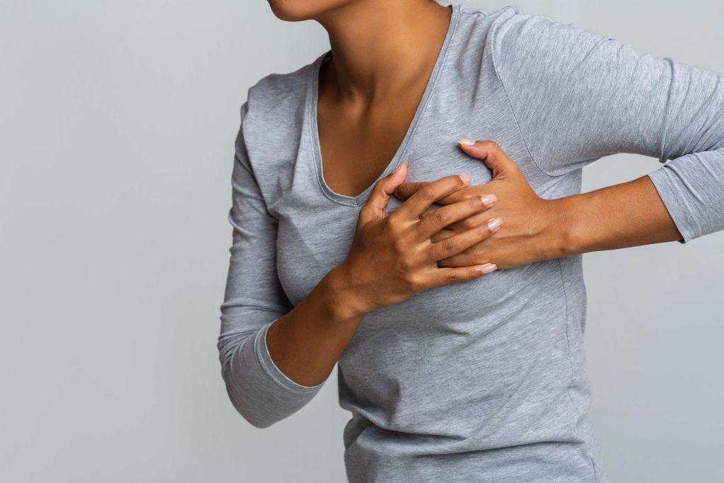 Woman wearing gray from the neck down clutching breast area.